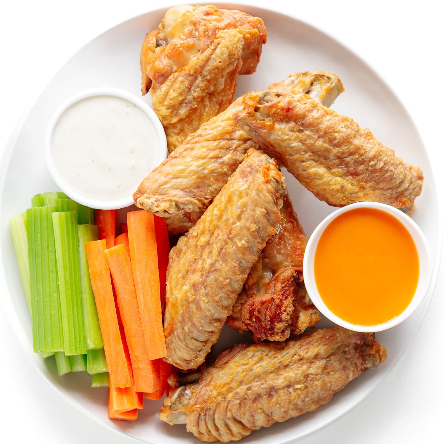 Baked turkey wings on a white plate with dipping sauces, carrot and celery sticks.