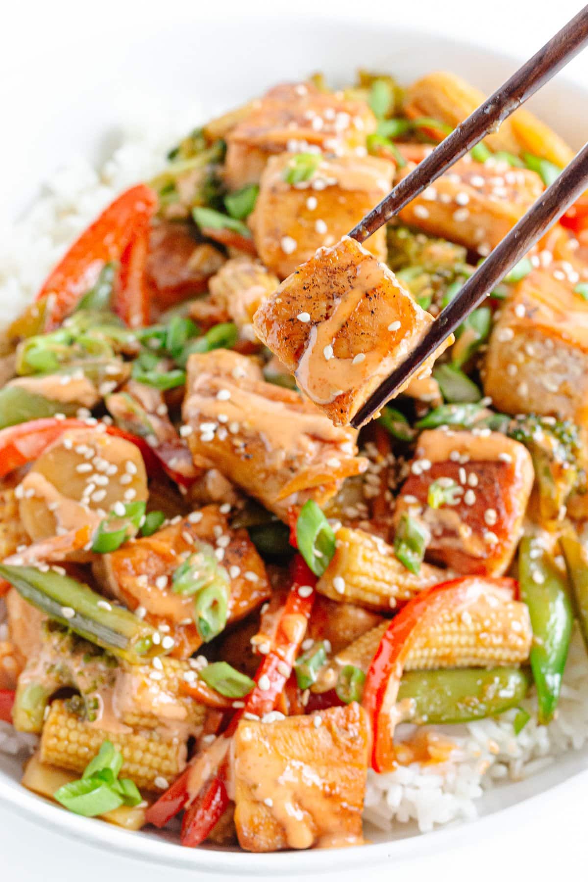 Chopsticks picking up a cube of salmon from a bowl of salmon stir fry.