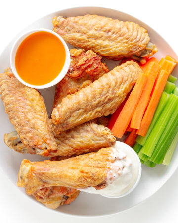 Crispy baked turkey wings on a white plate served with two dipping sauces, carrot and celery sticks.