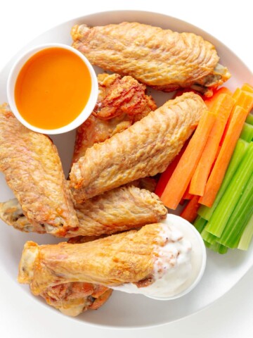 Crispy baked turkey wings on a white plate served with two dipping sauces, carrot and celery sticks.