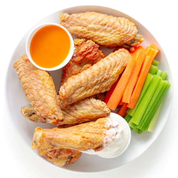 Crispy baked turkey wings on a white plate served with two dipping sauces, carrot and celery sticks.