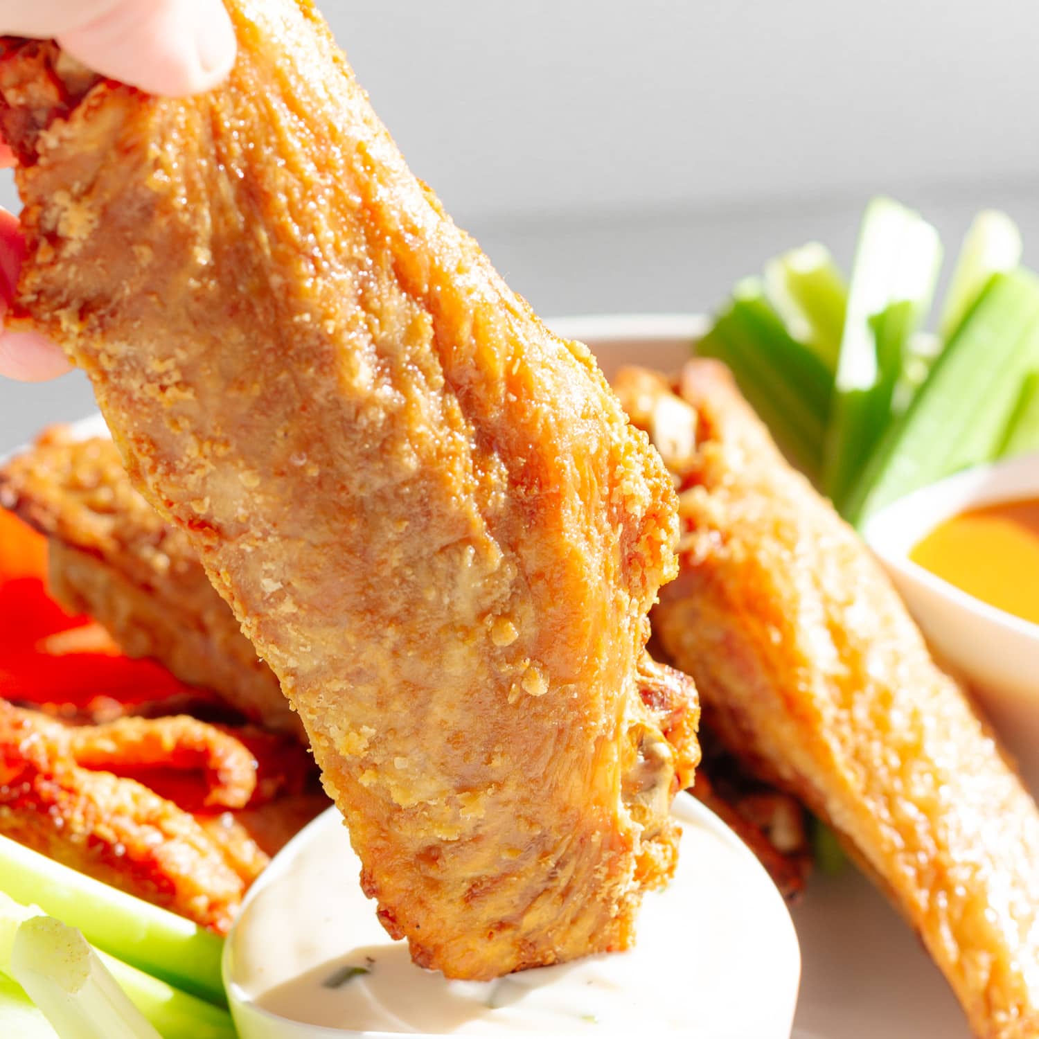 A turkey wing being dipped into blue cheese dressing.