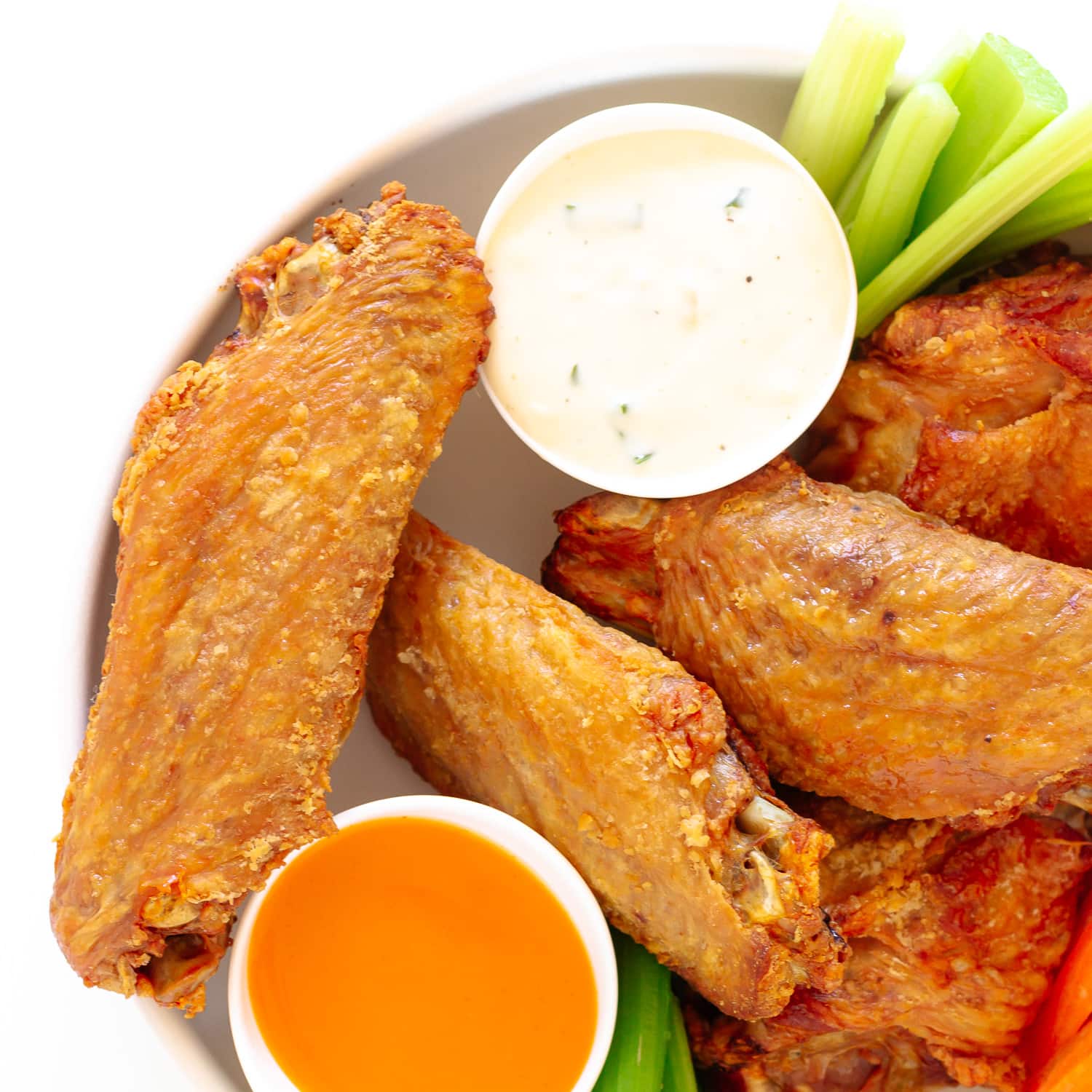 Closeup of crispy roasted turkey wings in a bowl with two dipping sauces.