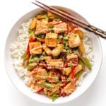 Salmon stir fry over a bed of rice in a white bowl with chopsticks positioned diagonally along the top.