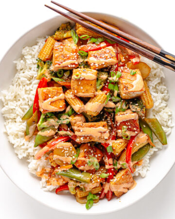 Salmon stir fry over a bed of rice in a white bowl with chopsticks positioned diagonally along the top.