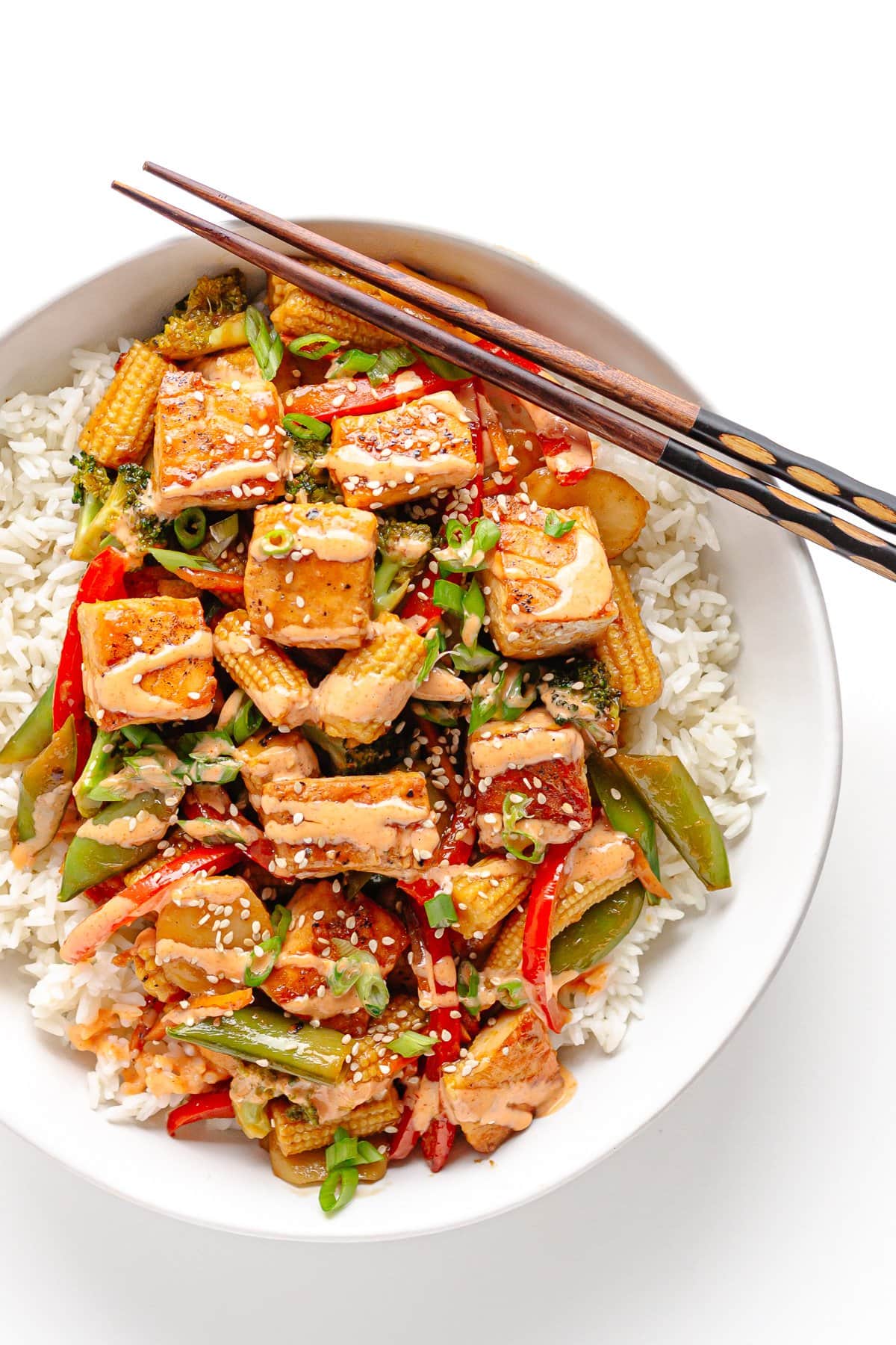 White bowl of rice topped with salmon stir fry and chopsticks positioned diagonally across the top.