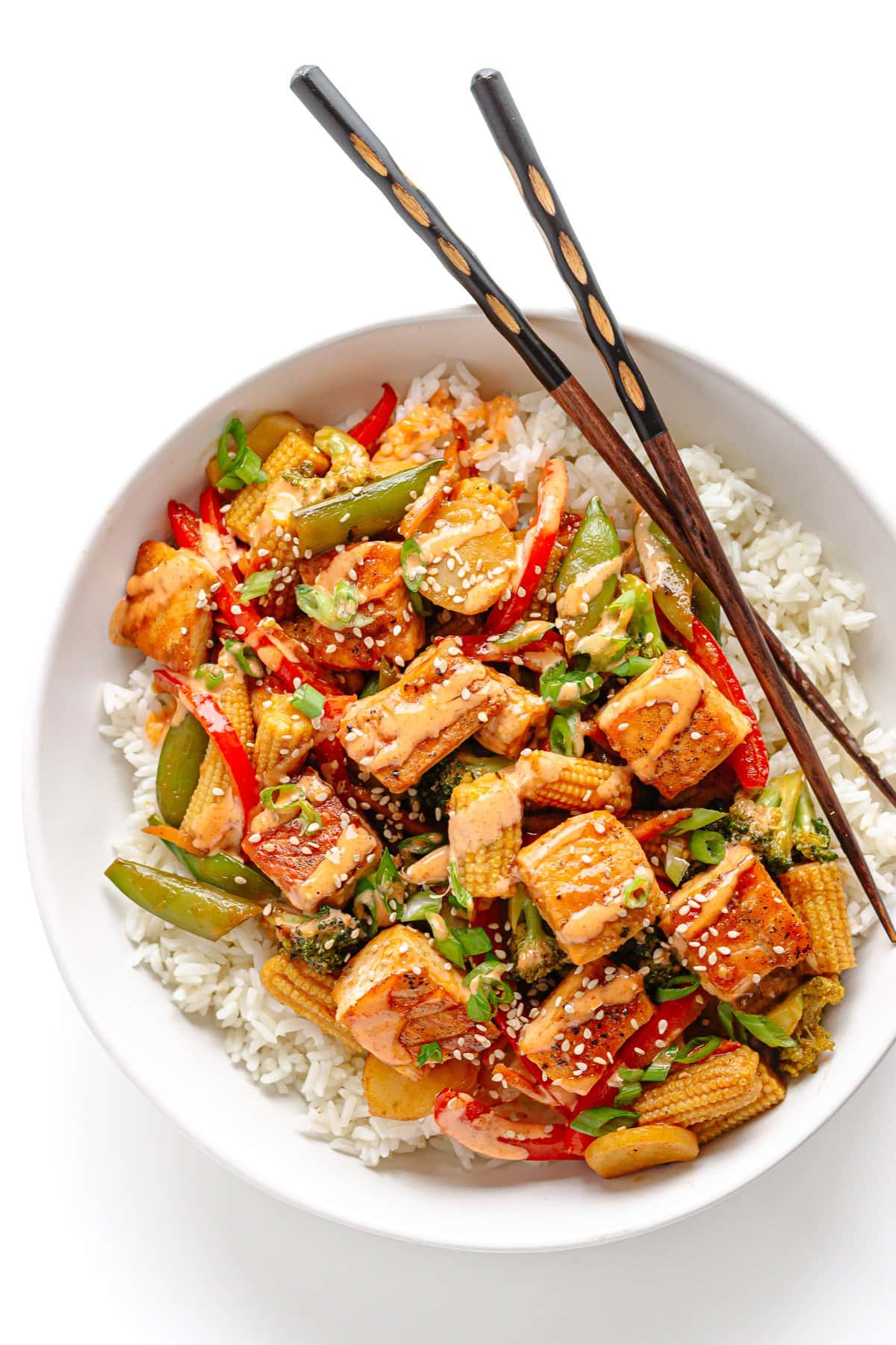 Salmon stir fry served over rice in a white bowl with chopsticks.