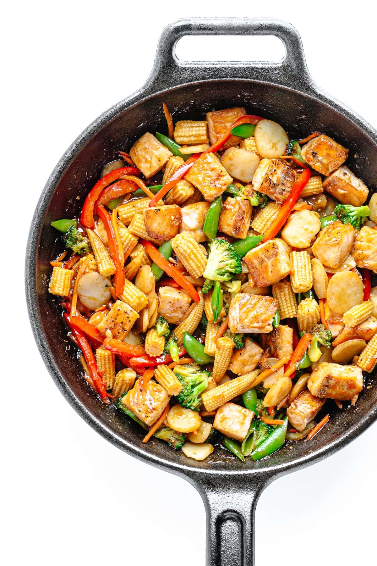 Overhead of salmon stir fry in a cast iron skillet on a white background.