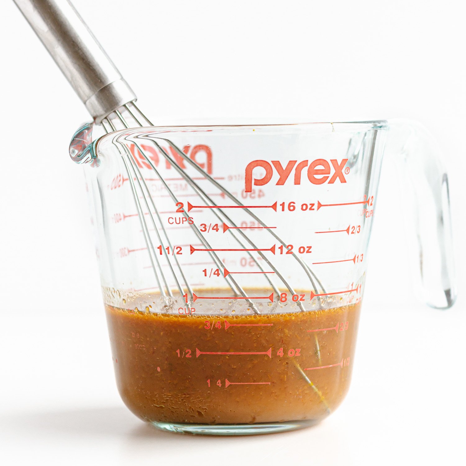 Glass measuring cup filled with homemade stir fry sauce and a whisk.