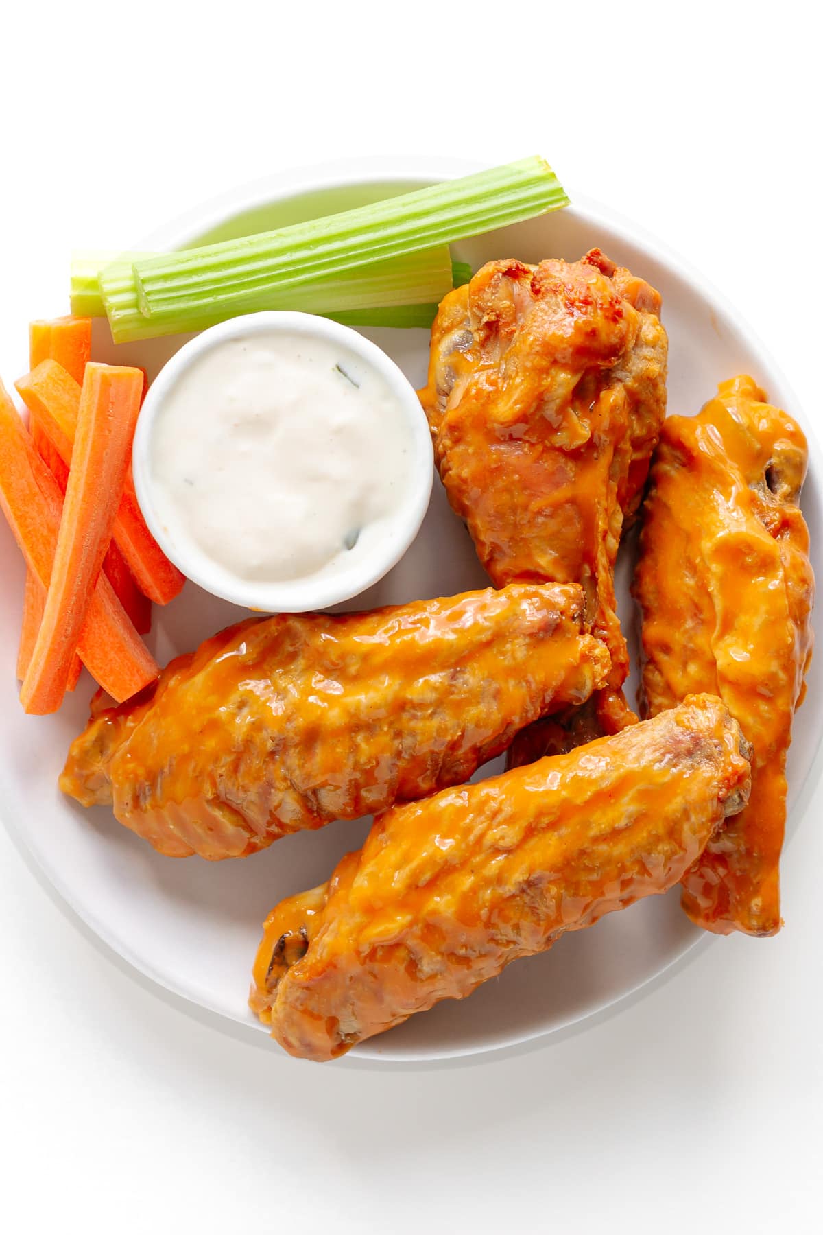 Split turkey wings tossed in buffalo wing sauce served on a white plate with blue cheese dressing, carrot and celery sticks.