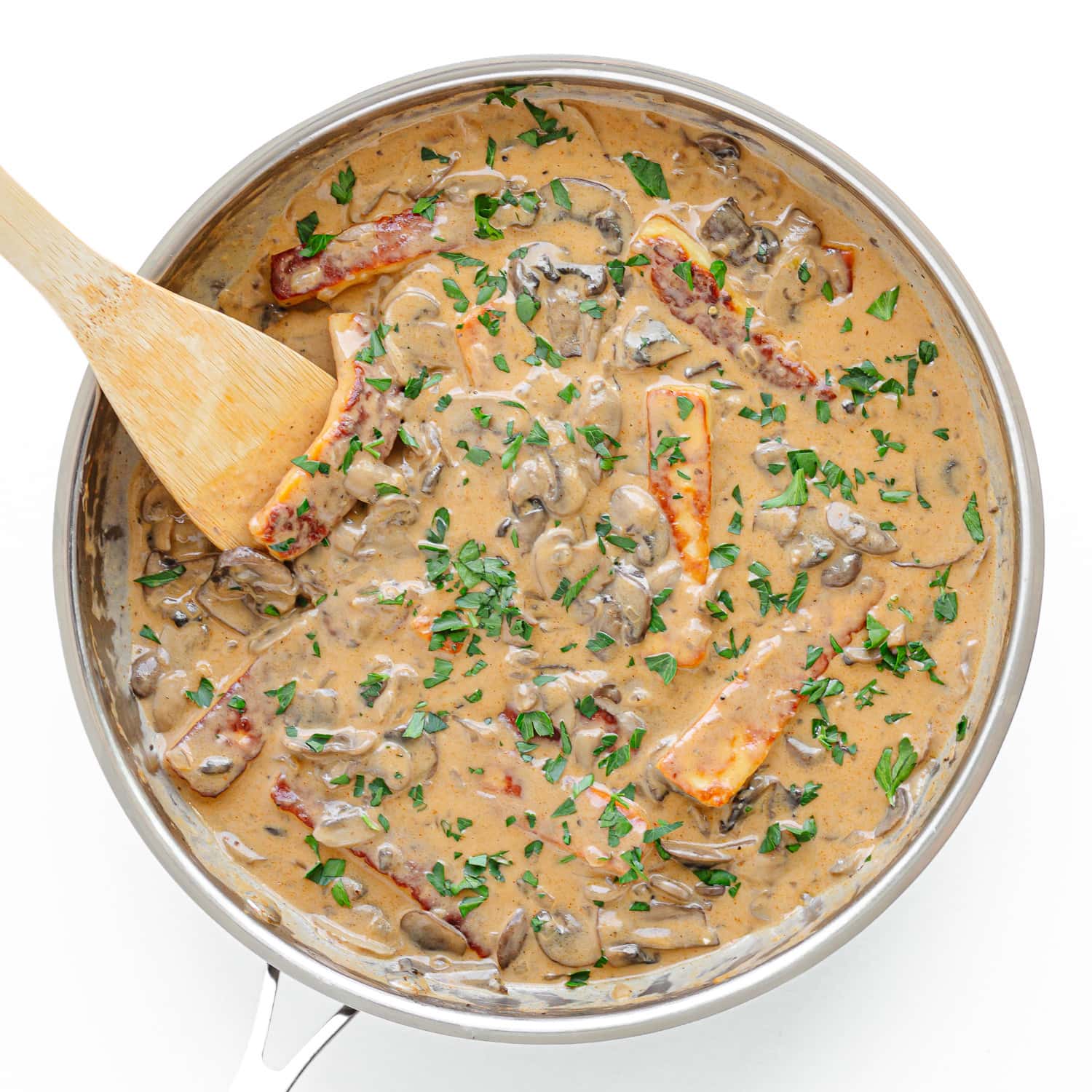 Halloumi Stroganoff in a stainless steel pan being stirred with a wooden spoon.