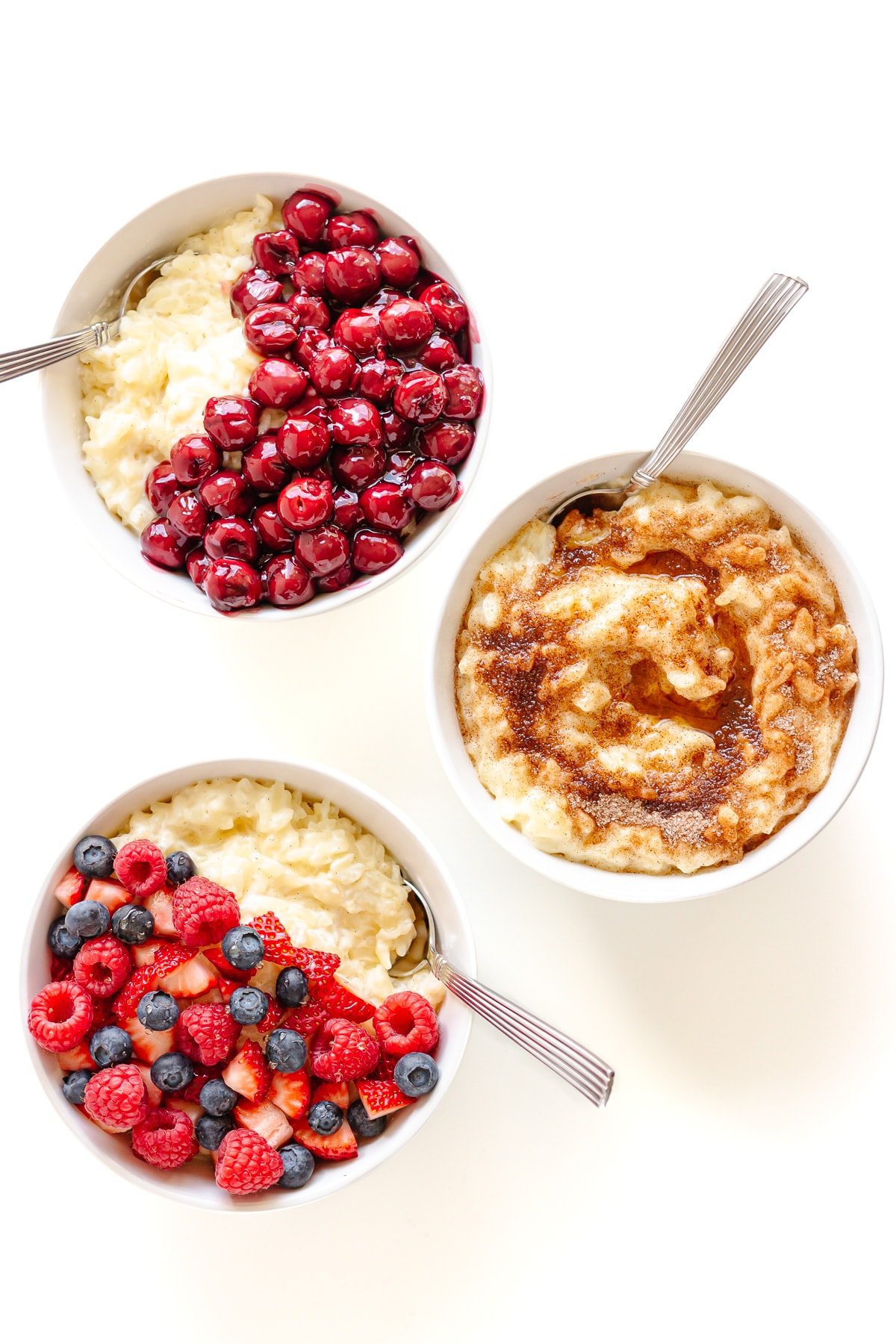 Three bowls of German Rice Pudding with different toppings displayed on a white background.