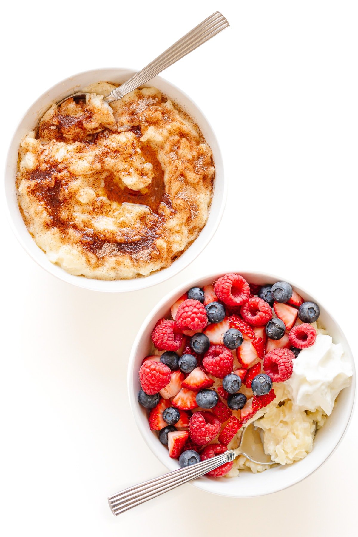Two bowls of Milchreis (German Stovetop Rice Pudding), one topped with cinnamon sugar and brown butter and the other topped with mixed berries and whipped cream.