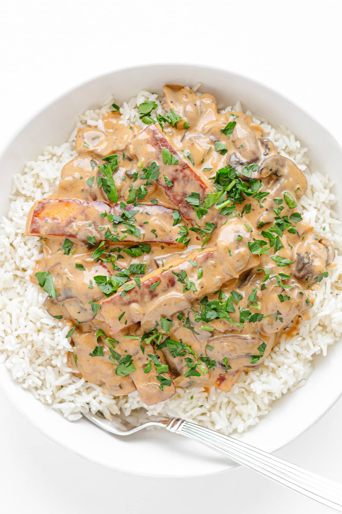 Halloumi Stroganoff served over rice in a white bowl with fork.