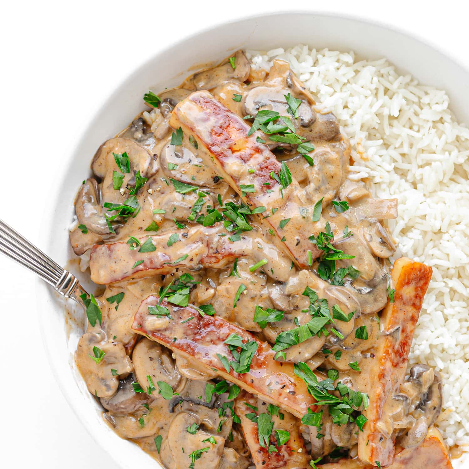 Halloumi Stroganoff served over rice in a white bowl.