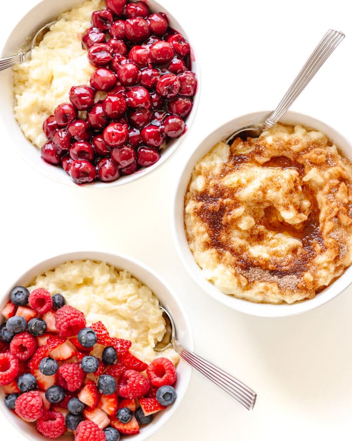 Three bowls of Milchreis (German Rice Pudding) with different toppings displayed on a white background.