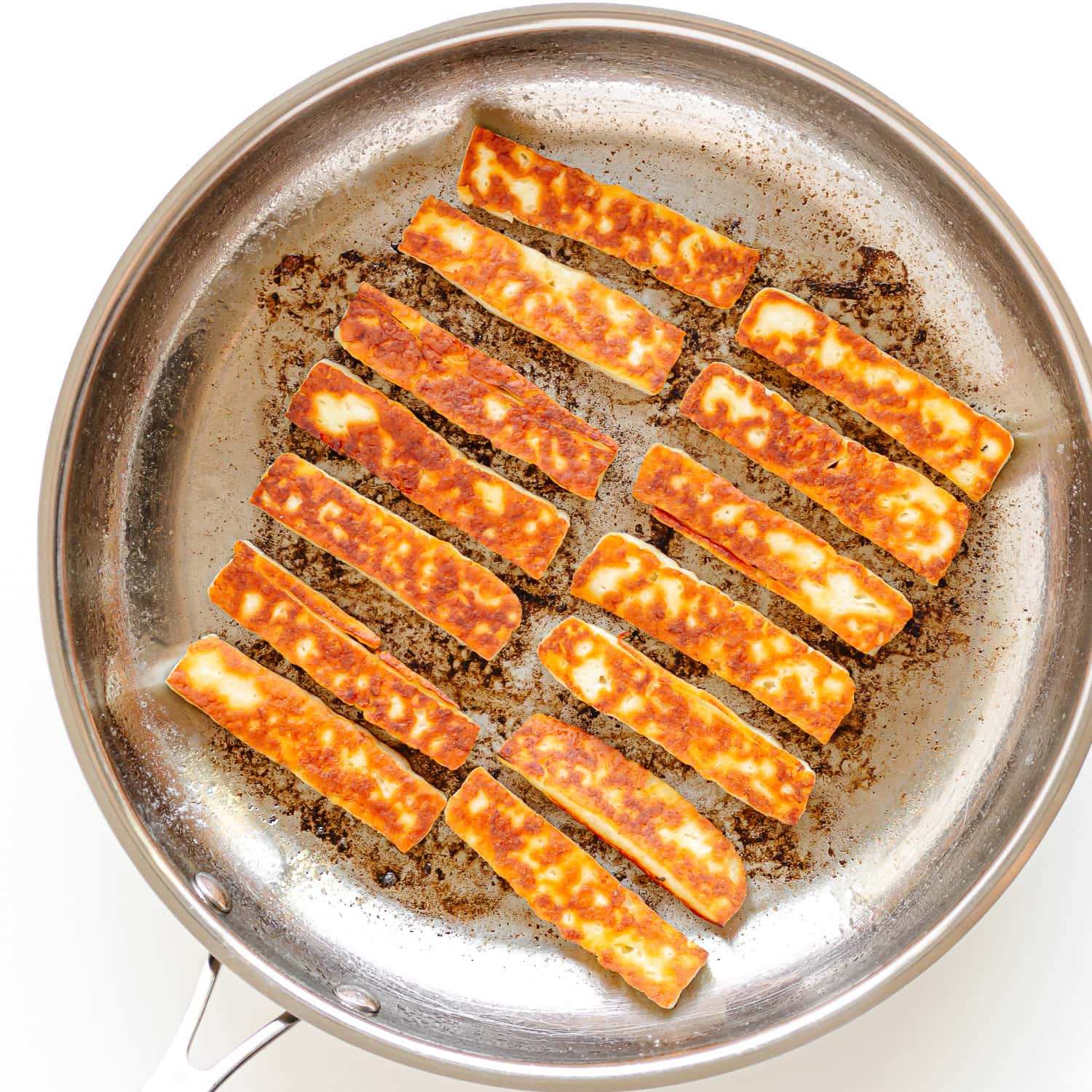 Strips of halloumi being pan fried in a stainless steel skillet.