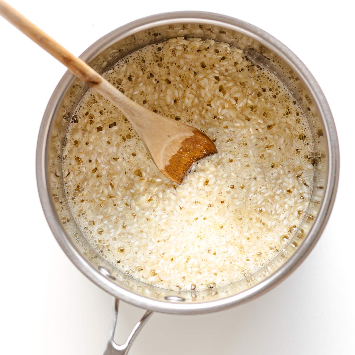 Uncooked arborio rice being sautéed in butter in a large stainless steel saucepan. 