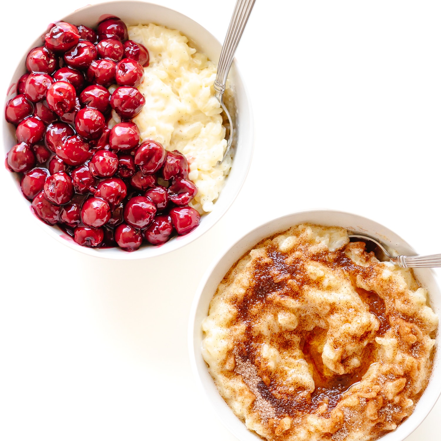 Two bowls of Milchreis/Reisbrei (German Rice Pudding), one topped with warm cherries and the other with cinnamon sugar and brown butter.