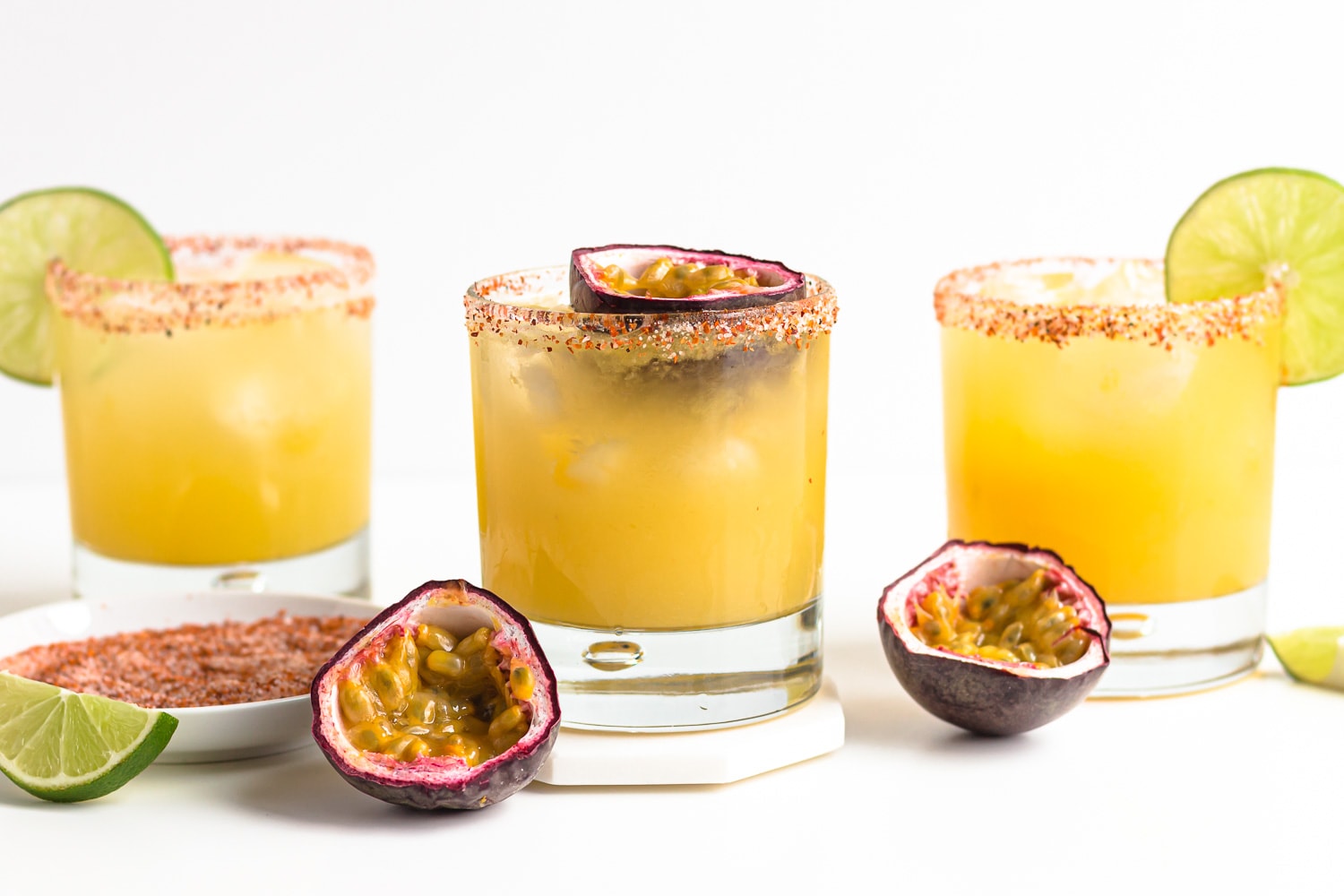 Three garnished glasses of passion fruit margarita cocktails on a white background.