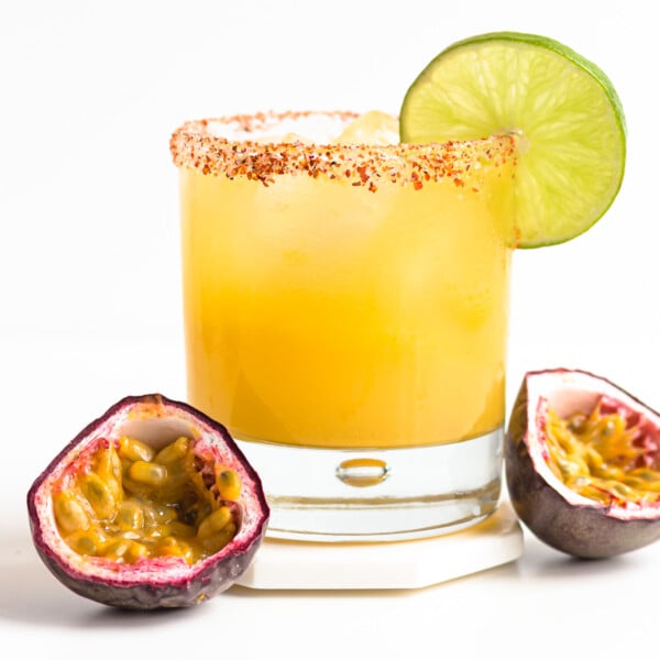 A glass of passion fruit margarita garnished with a lime slice and two passion fruit halves sitting beside it.