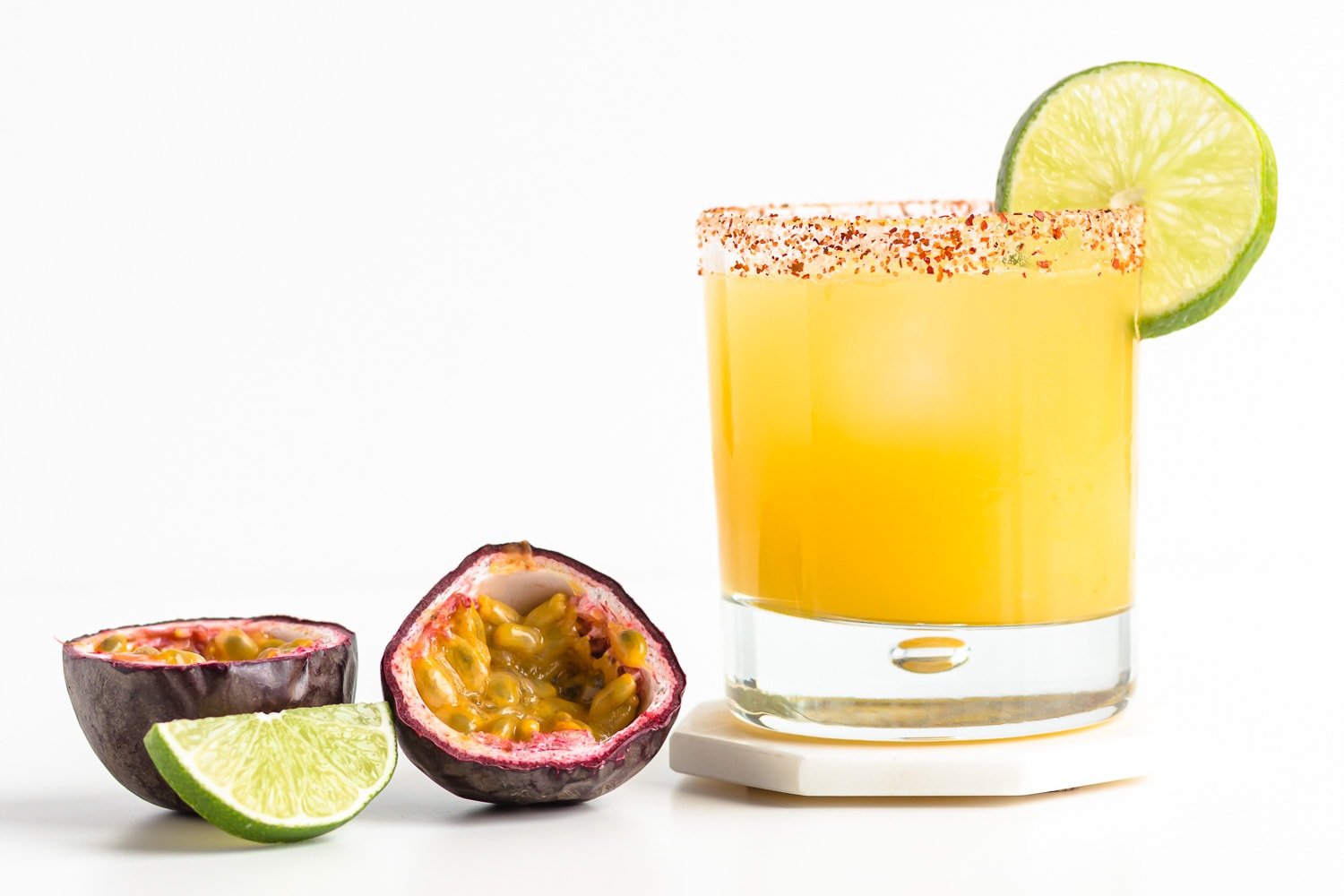 A passion fruit margarita with two passion fruit halves and a lime wedge beside it.