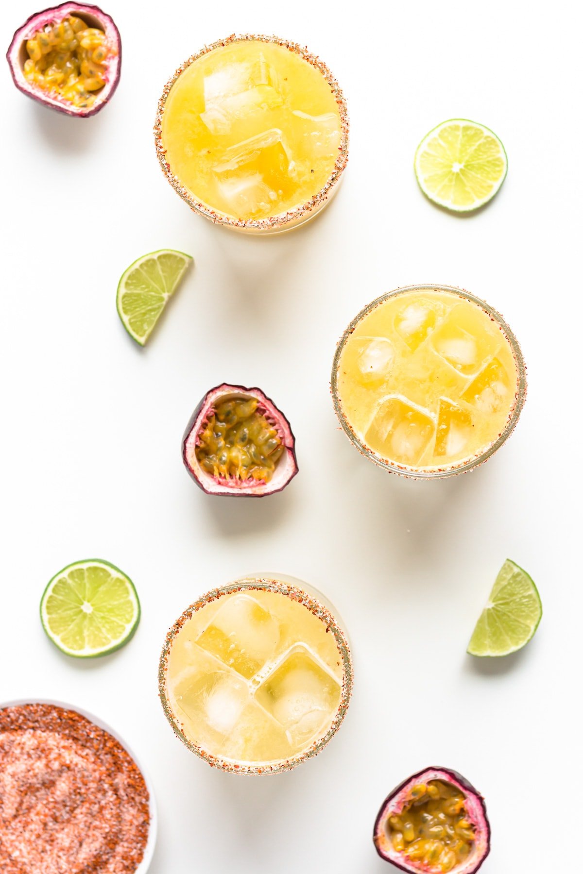 Overhead photo of three passion fruit margaritas with garnishes scattered next to them.