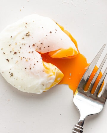A poached egg that has been broken into with a fork to reveal the runny yolk.