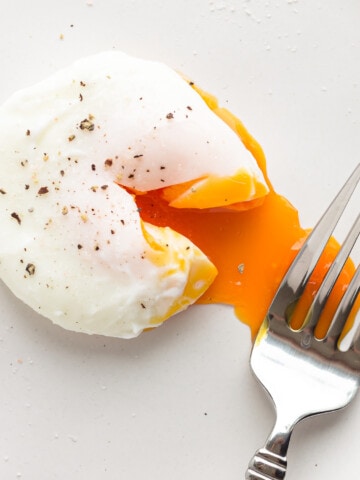 A poached egg that has been broken into with a fork to reveal the runny yolk.