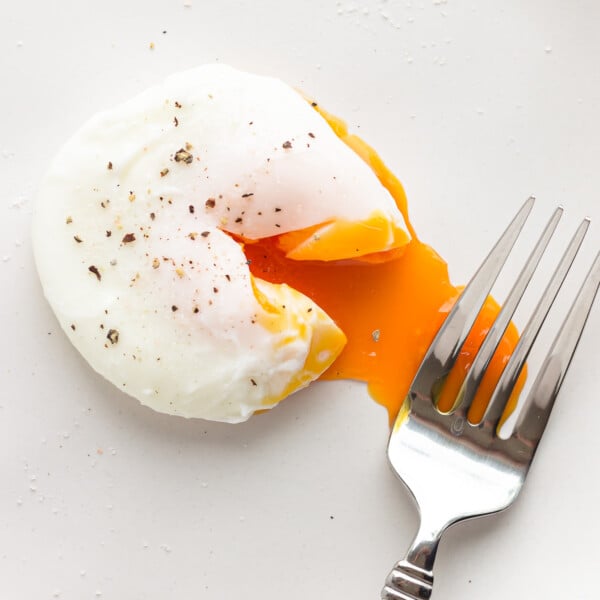 A poached egg that has been broken into with a fork to reveal the runny yolk.