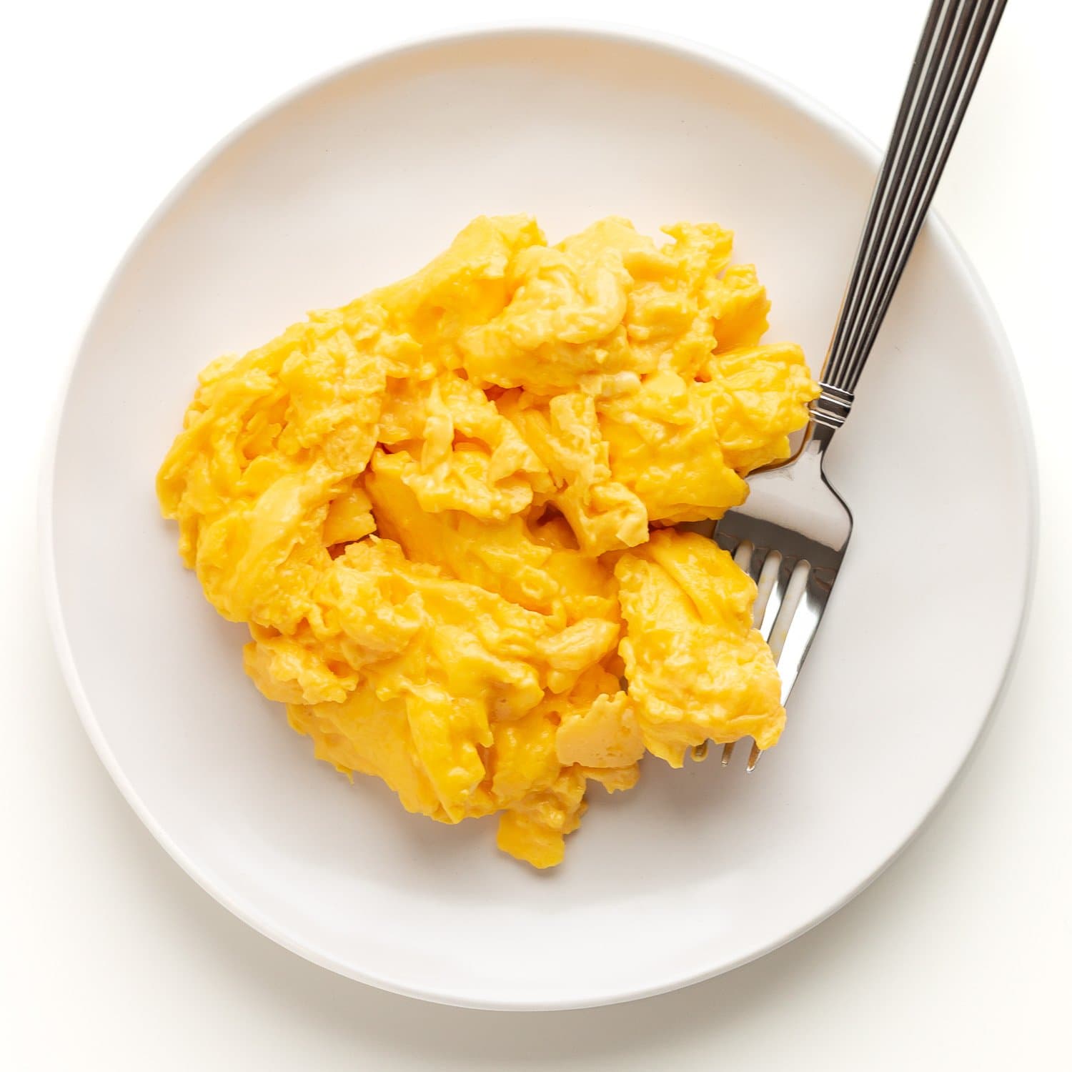 A plate full of scrambled eggs with a fork.