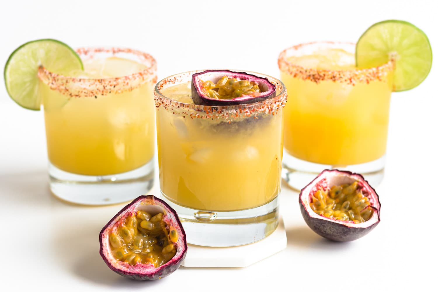 Three passion fruit cocktails garnished with lime slices and passion fruit halves.