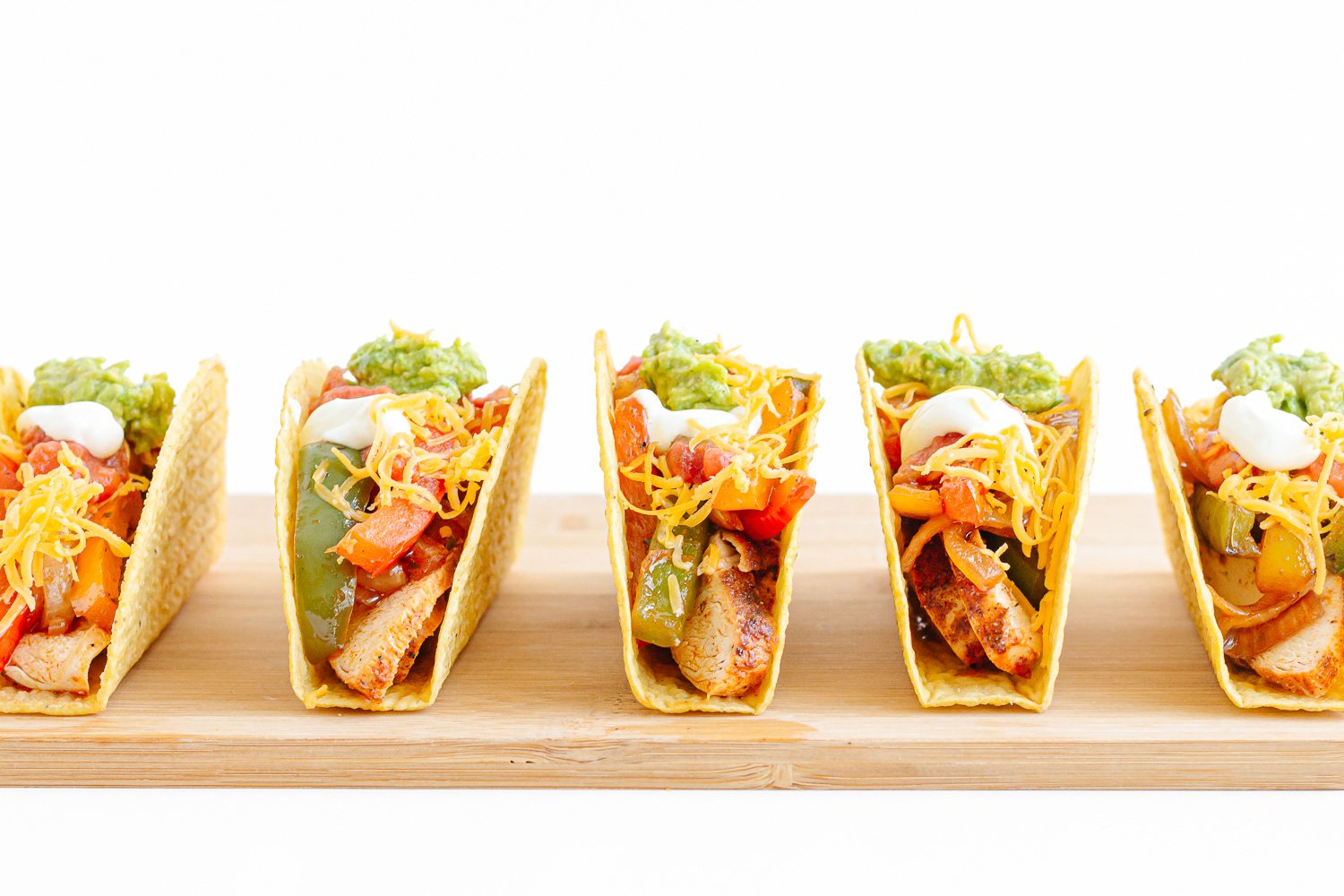 Side view of crunchy hard shell tacos lined up on a wooden board against a white background.