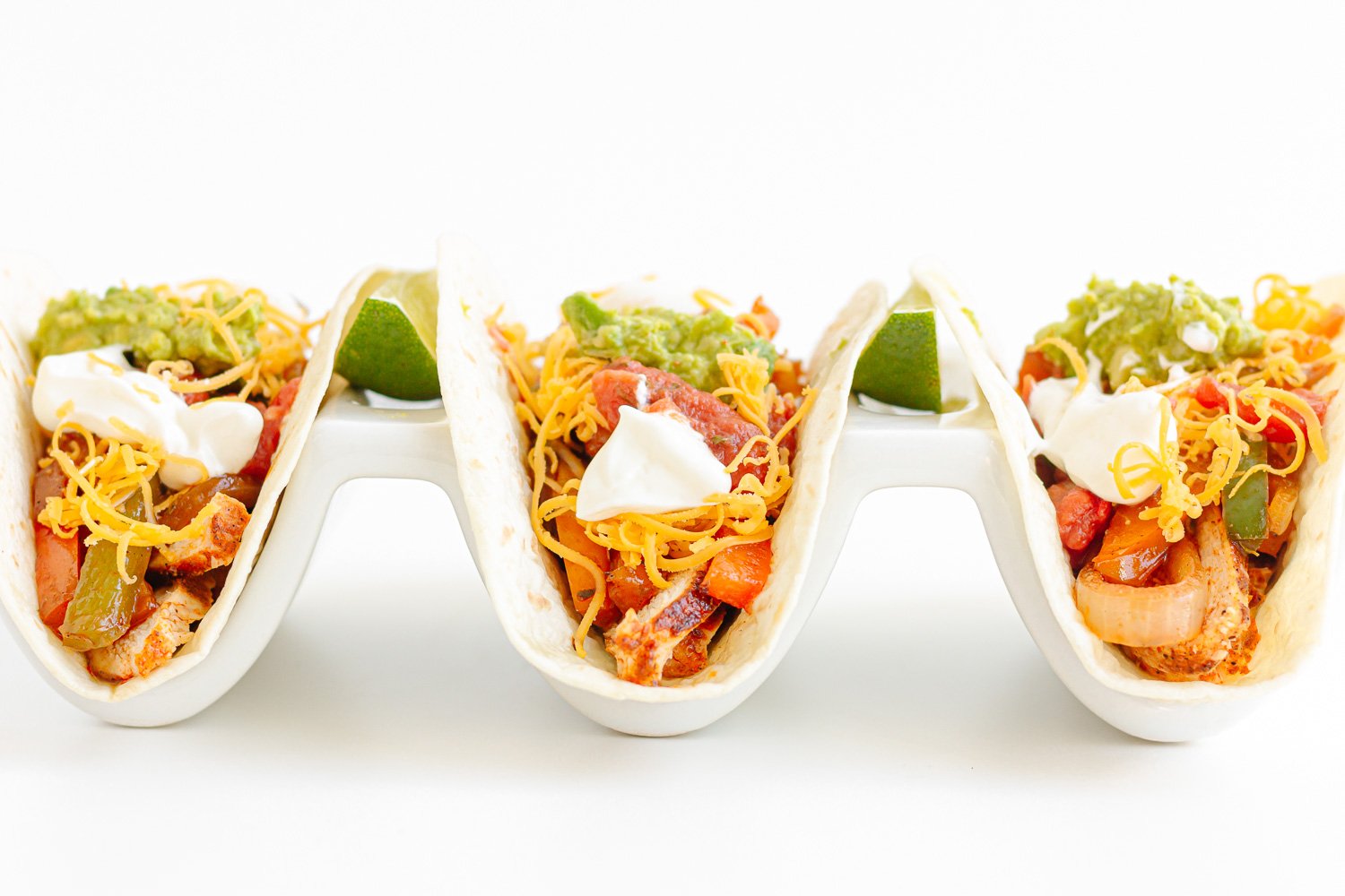 Side view of three chicken fajita tacos served in soft tortillas in a white taco holder.
