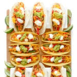 Twelve chicken fajita tacos on a wooden board, some served in soft tortillas and some in crunchy taco shells.