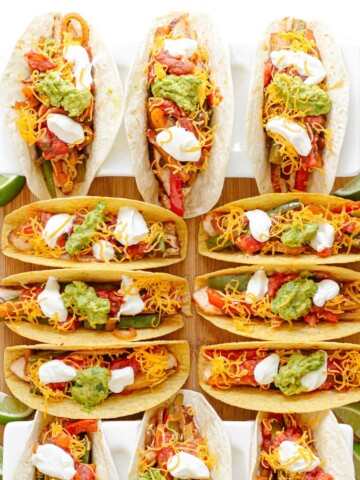 Twelve chicken fajita tacos on a wooden board, some served in soft tortillas and some in crunchy taco shells.