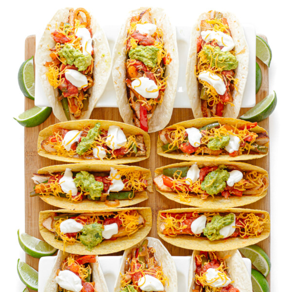 Twelve chicken fajita tacos on a wooden board, some served in soft tortillas and some in crunchy taco shells.