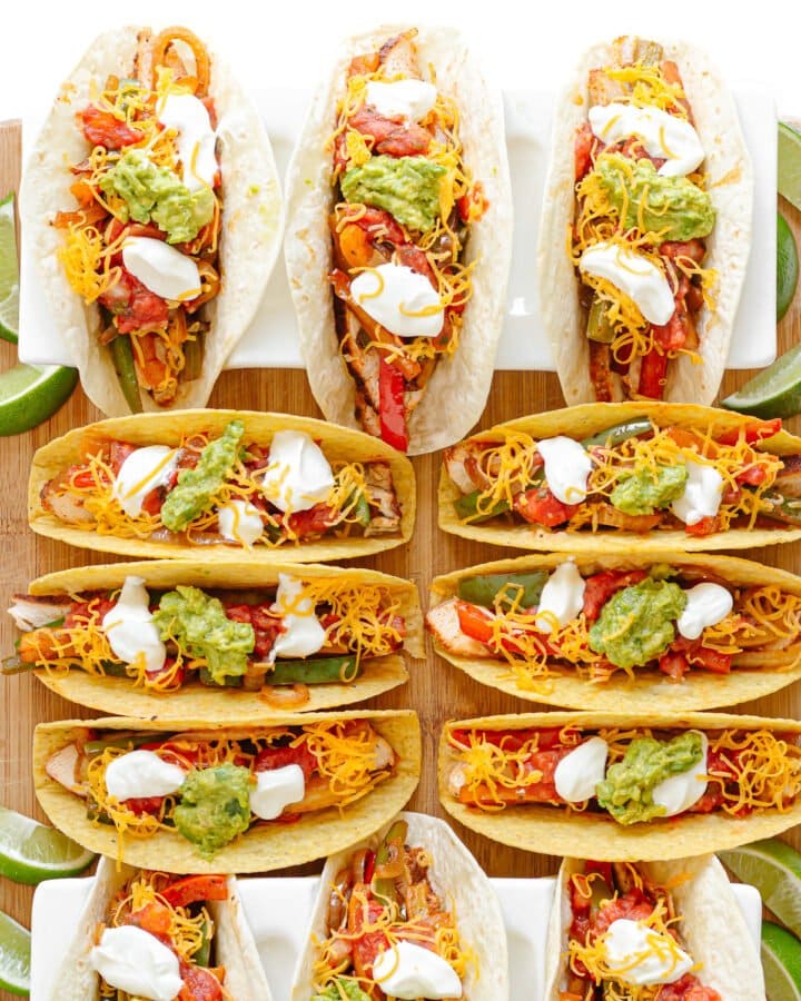 Twelve chicken fajita tacos on a wooden board, some served in soft tortillas and some in crunchy taco shells.