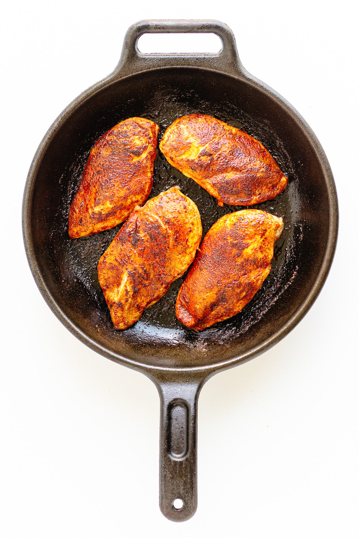 Four seared chicken breasts in a cast iron skillet.