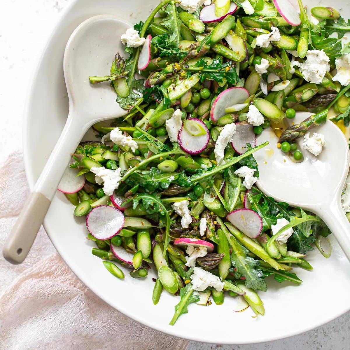 Asparagus salad with goat cheese and sliced radishes in a serving bowl.