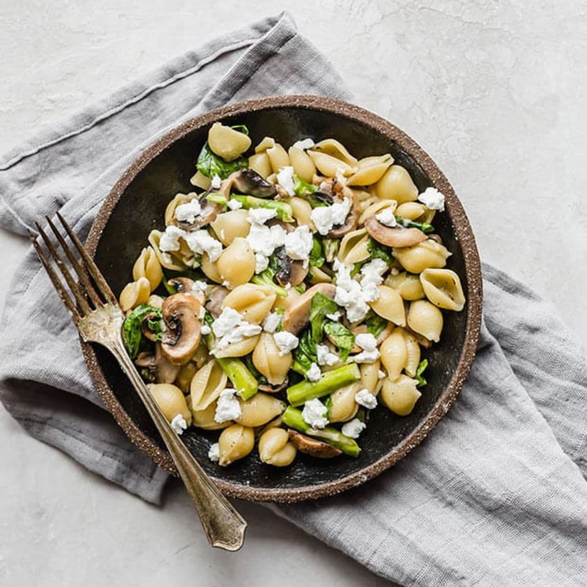 Bowl of pasta with asparagus, spinach, mushrooms and goat cheese.
