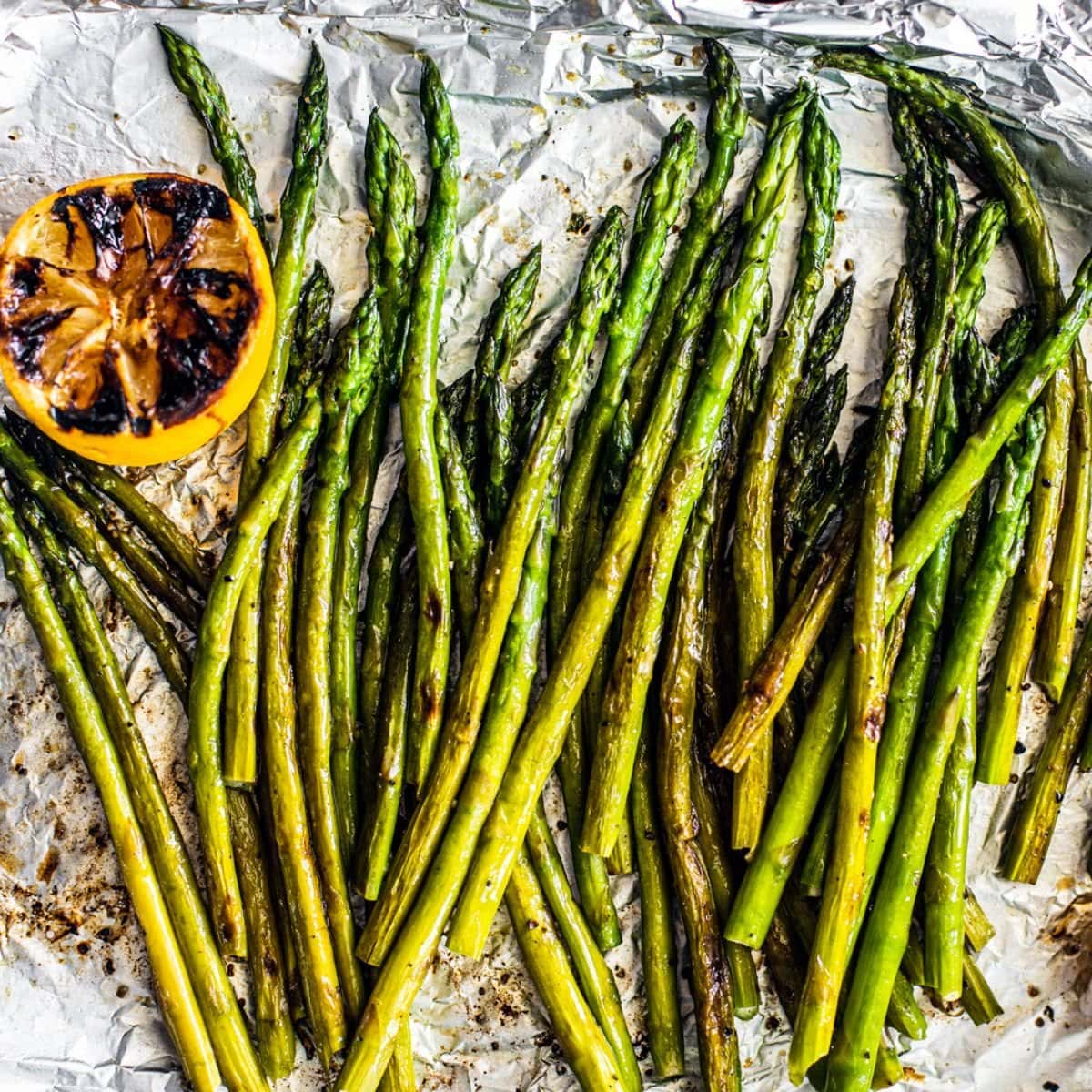 Grilled asparagus with a charred lemon half sitting on a sheet of foil.