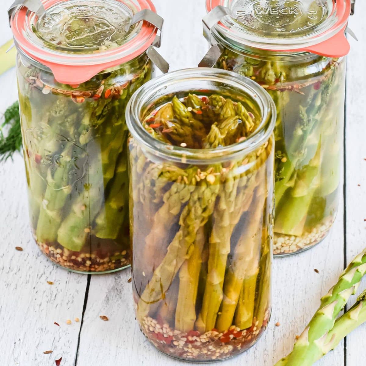 Three glass jars of pickled asparagus.