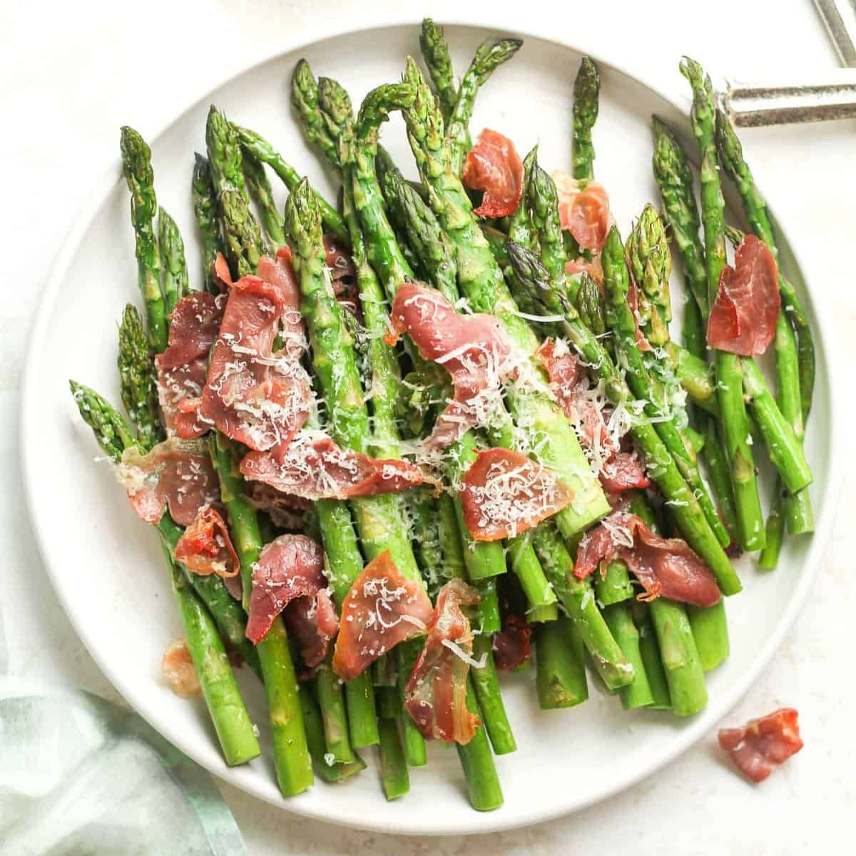 Roasted asparagus with crispy prosciutto and shredded parmesan on a serving plate.