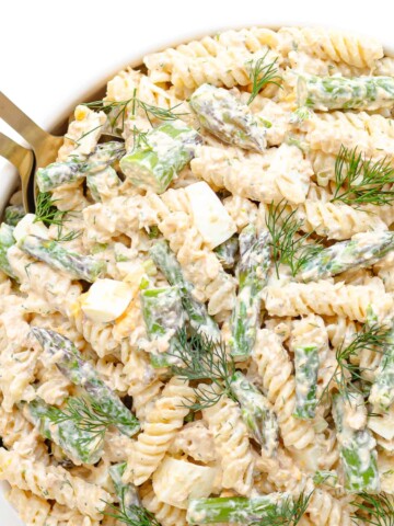 Salmon and asparagus pasta salad with a creamy lemon dill dressing in a white serving bowl with gold salad servers.