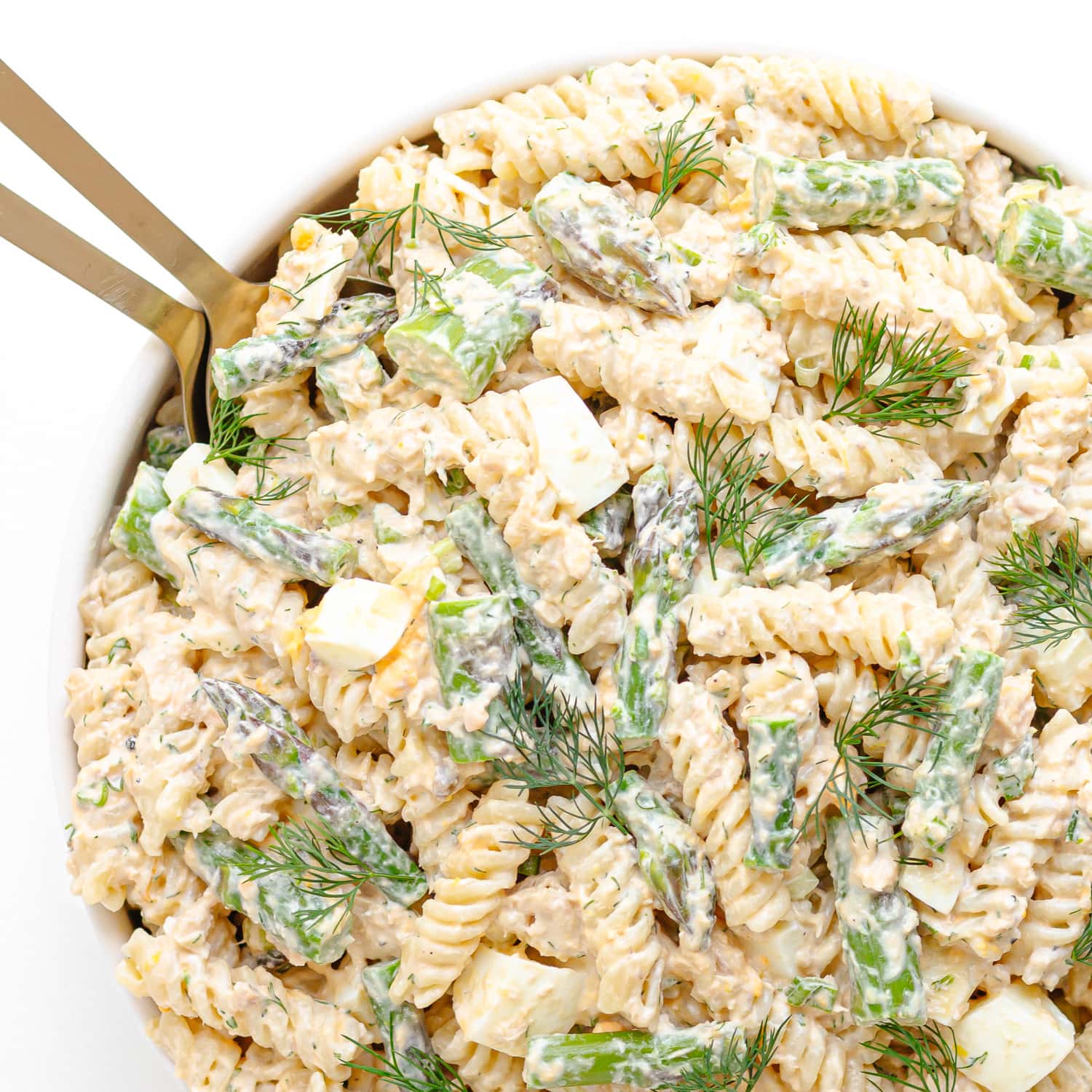 Salmon and asparagus pasta salad with a creamy lemon dill dressing in a white serving bowl with gold salad servers.