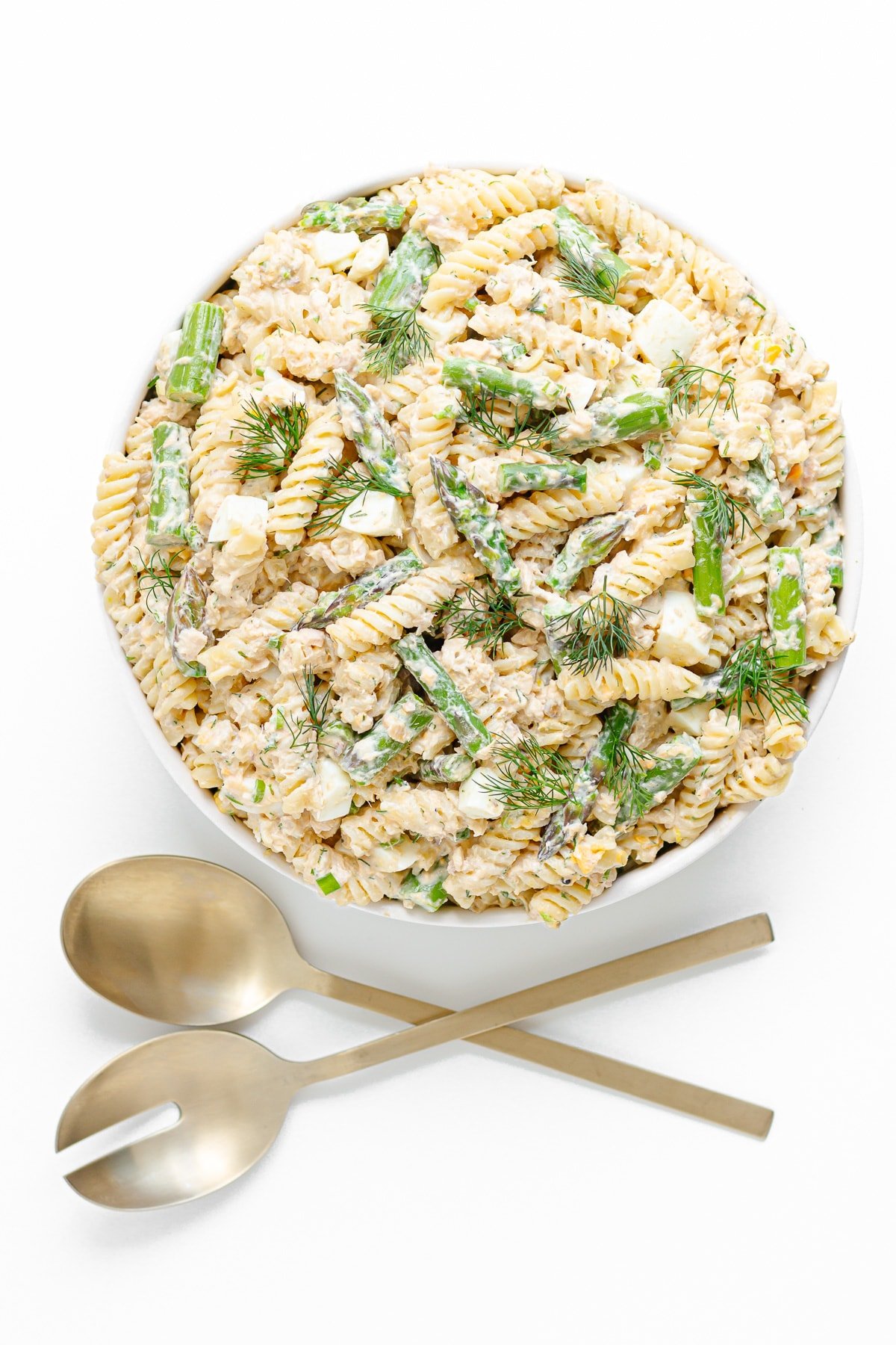 Salmon pasta salad in a white serving bowl with gold salad servers sitting below the bowl.