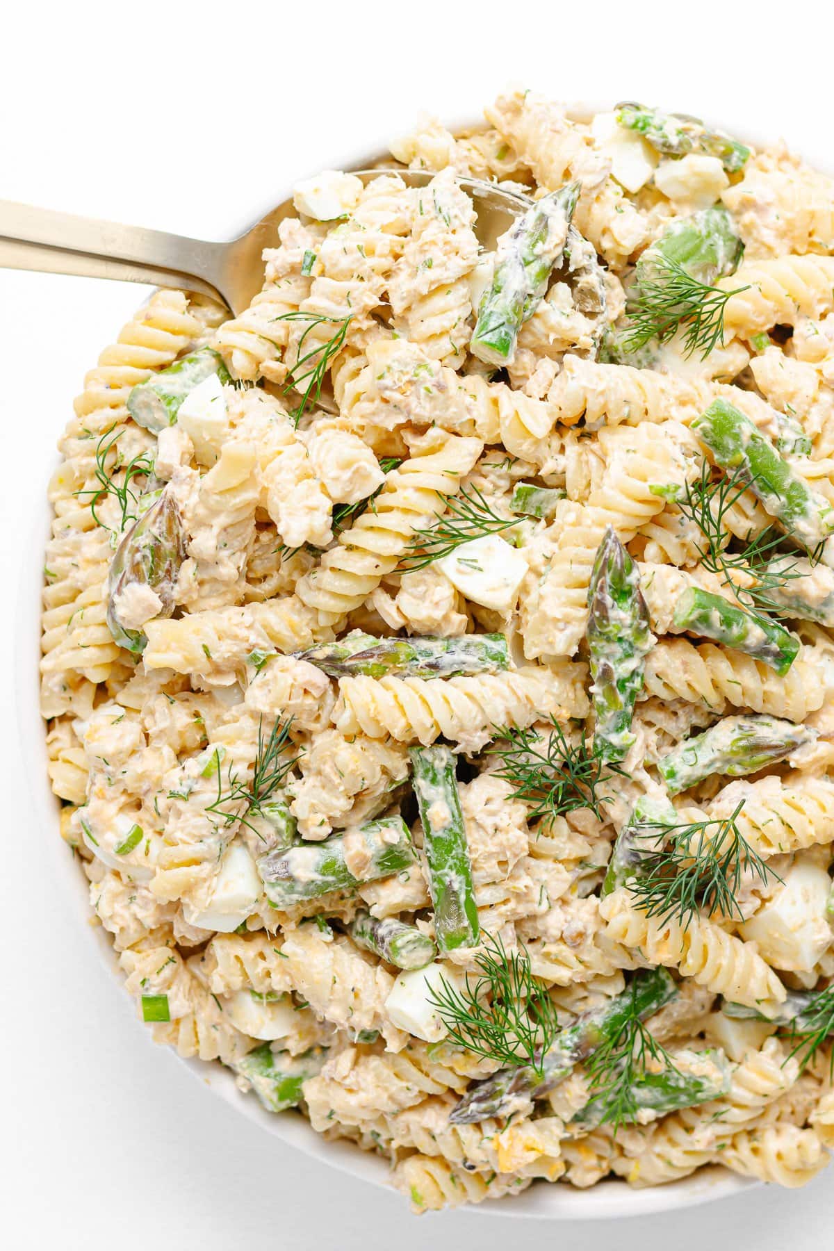 Salmon pasta salad in a white serving bowl with gold colored salad servers.