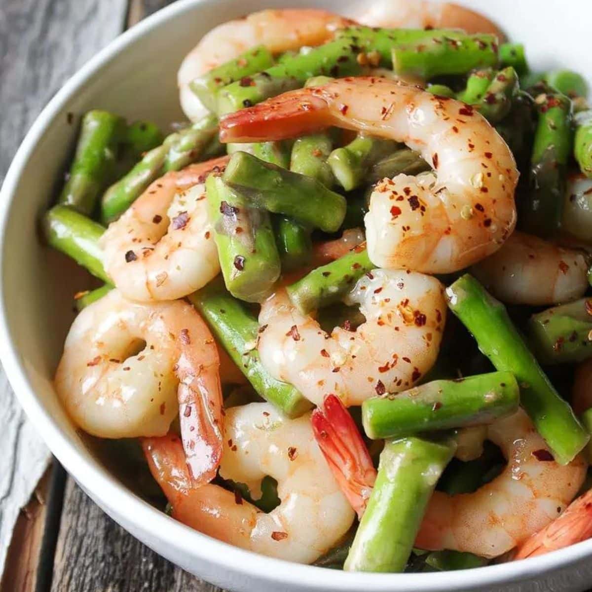 Shrimp and asparagus stir fry in a white bowl.