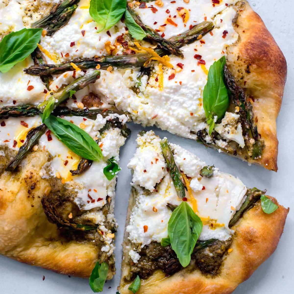 Pizza topped with pesto, grilled asparagus, lemon zest and fresh basil leaves.ricotta, burrata
